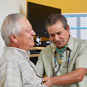 A healthcare worker holds a stethoscope to a smiling older person