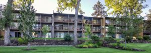 View of the front of a multifamily apartment building with trees and grass in foreground.