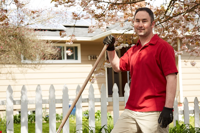 Man standing in front of his home with a rake in hand