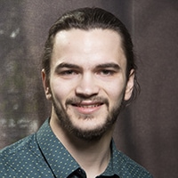 a bearded young person with hair pulled back looking at the camera