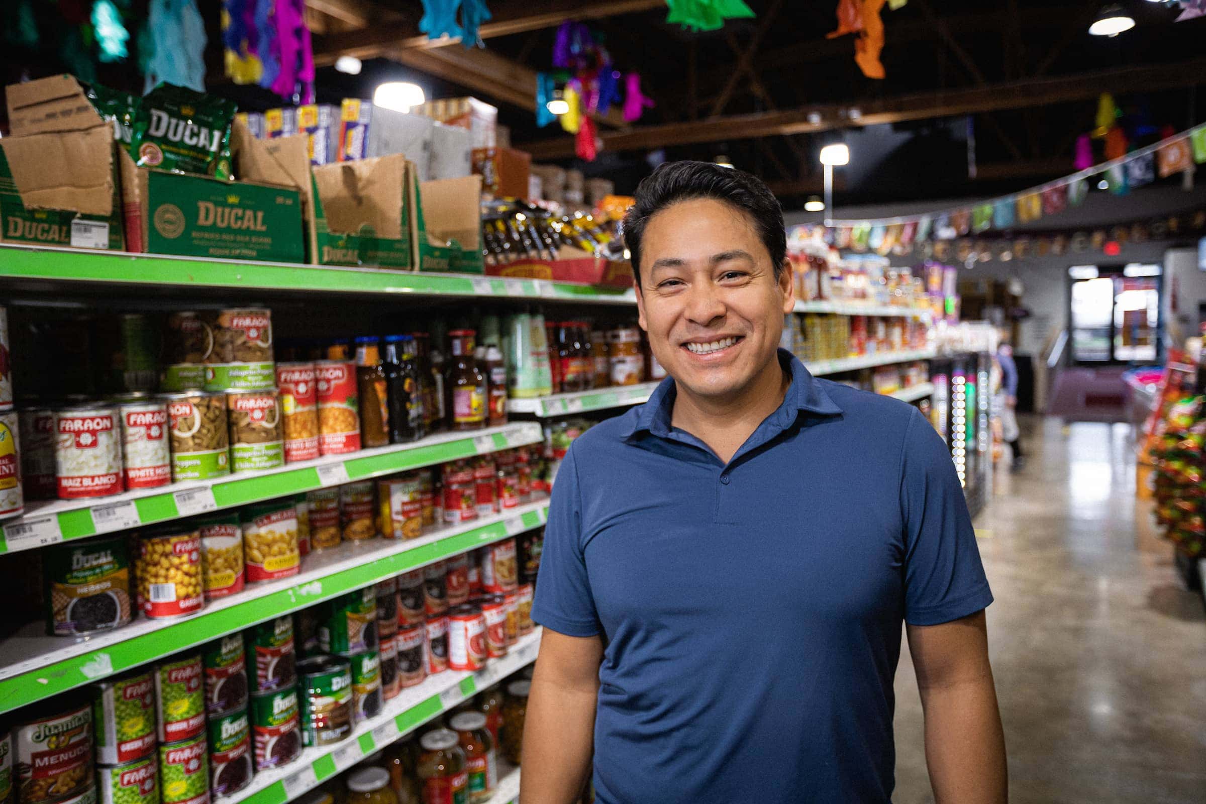 A man smiling to the camera in front of a grocery store shelf.
